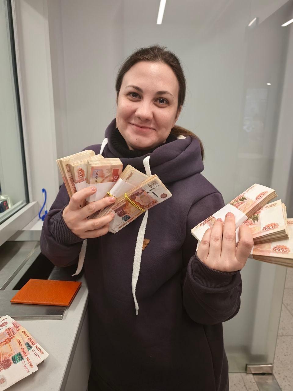 Женщина улыбается и держит в руках наличные деньги